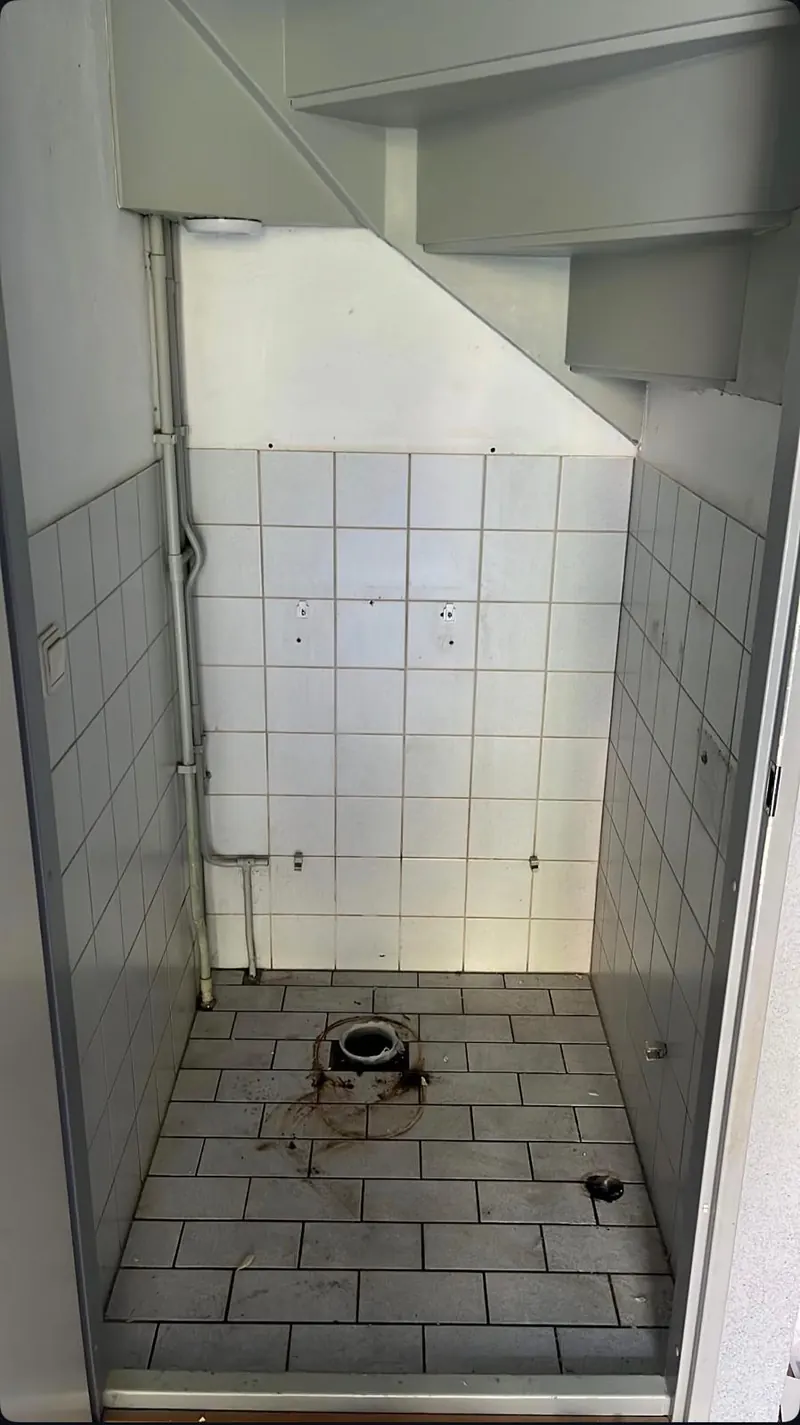 Toiletruimte onder de trap met oude tegels; het toilet is verwijderd