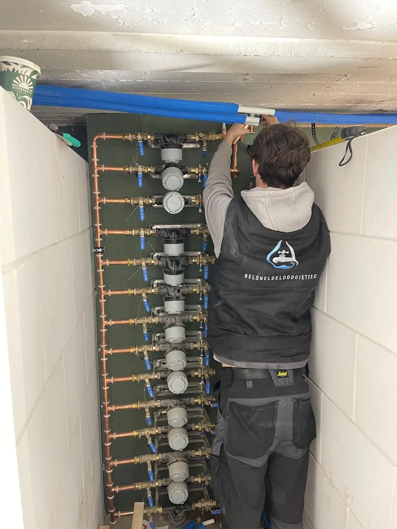 Monteur van Belsneldeloodgieter aan het werk bij een rij watermeters